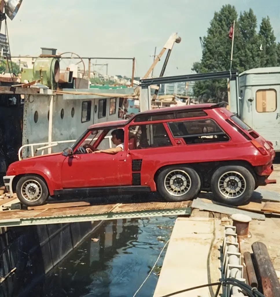 Renault 5 Turbo 6x6 positioned on a makeshift ramp near a dockyard, emphasizing its extended frame and off-road capabilities