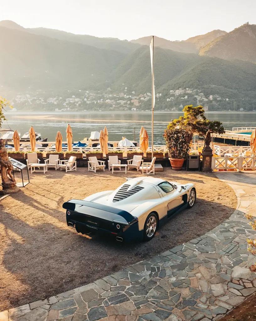 Stunning side profile of the Maserati MC12 by a scenic waterfront, highlighting its sleek curves and performance-focused stance